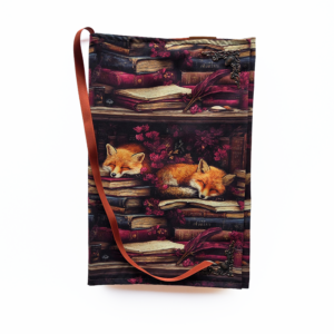 Boekenhoes - Slapende vos op paars is een leuke katoenen stof met een slapende vos bovenop boeken. De achtergrond is paars en heeft paarse bloemen. De binnenkant is briquekleurig, net zoals het leeslint. Het elastiek is in het bruin.