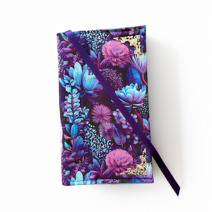 Een boekenhoes gemaakt van de stof Bahjou. Er zit een bloemenpatroon op in het paars met blauw.