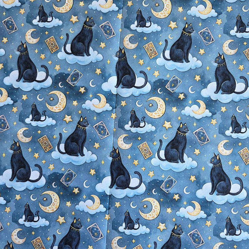Een katoenen stof met zwarte katten die op wolken zitten. Eromheen zitten tarotkaarten en halve maantjes. De achterkant is staalblauw.